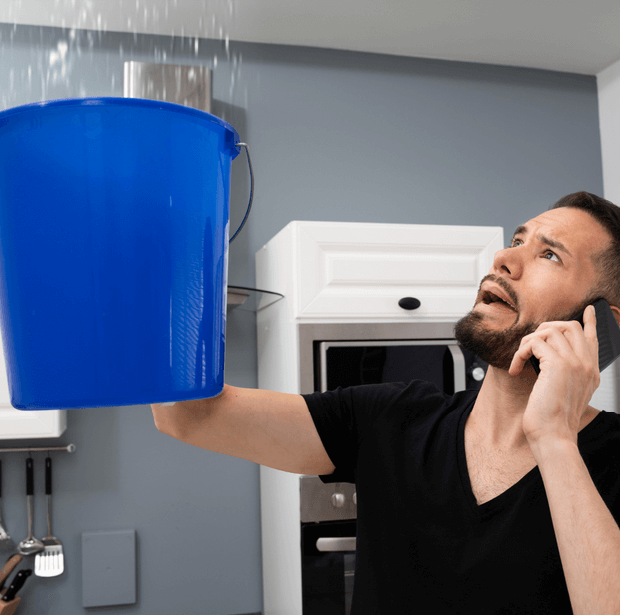 Homeowner catching a ceiling leak in a bucket while calling for water damage help